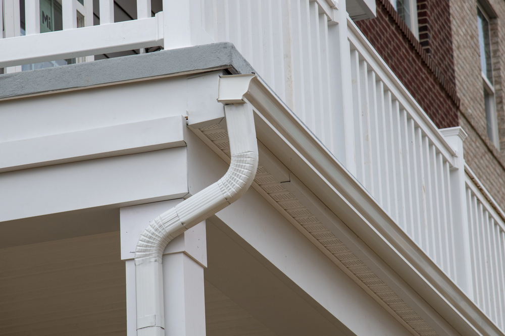 Close-up of a white downspout attached to the gutter of a white porch railing on a residential building.
